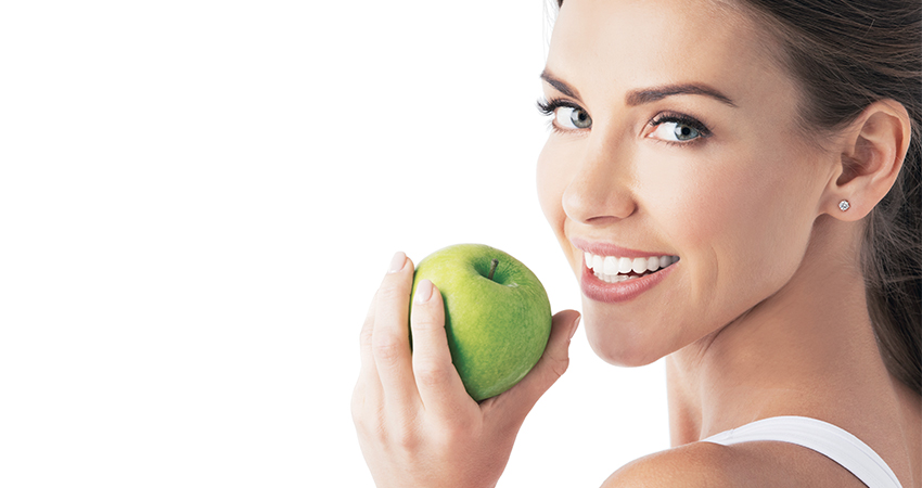 a 30-something woman with a complete smile, looking over her shoulder and about to bite into a green apple.