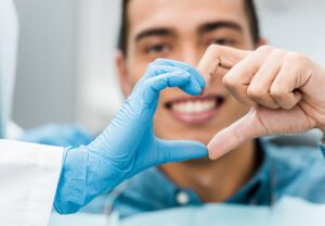 Two dentists making a heart sign with their fingers and the male dentist smiling